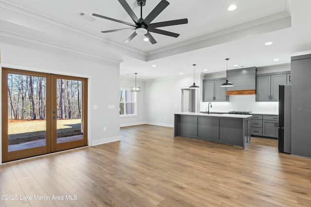 kitchen with light countertops, hanging light fixtures, an island with sink, and gray cabinetry