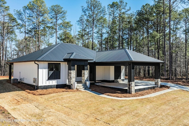 view of front facade with metal roof, a carport, stone siding, driveway, and a front lawn