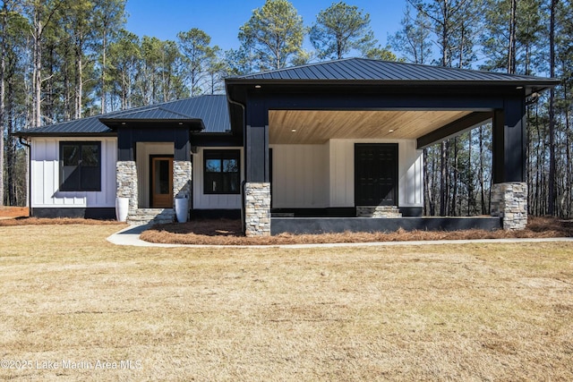 view of front of property featuring board and batten siding, stone siding, metal roof, and a front lawn