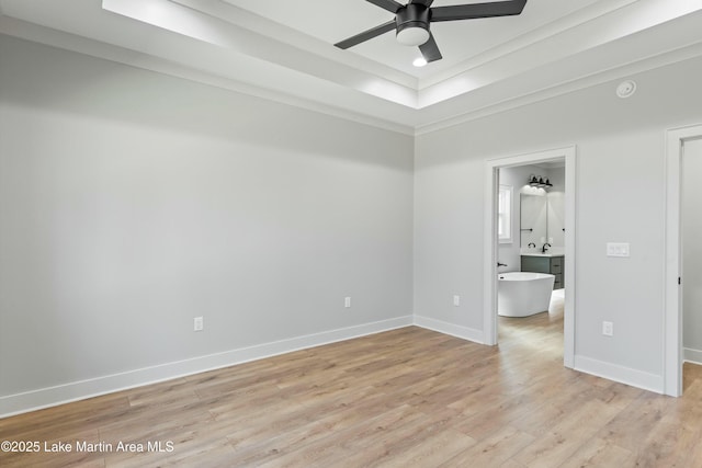 unfurnished bedroom featuring light wood-style flooring, baseboards, a raised ceiling, and ensuite bathroom