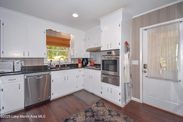 kitchen with white cabinetry, a warming drawer, dark countertops, appliances with stainless steel finishes, and a sink
