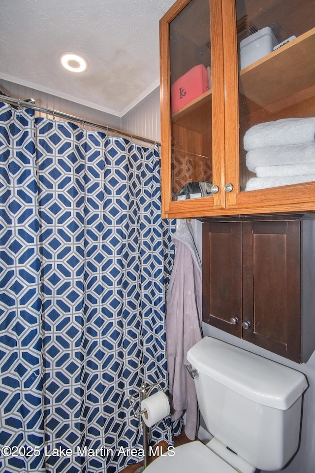 bathroom featuring toilet, tiled shower, and ornamental molding