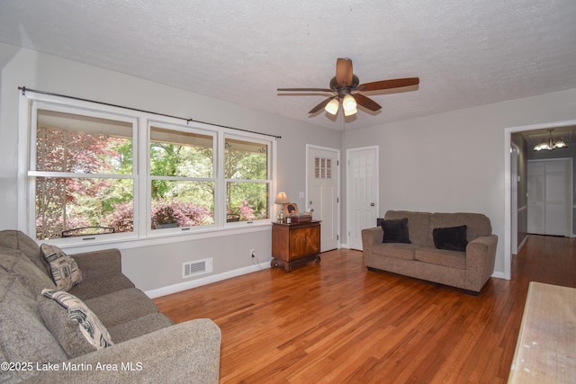 living area featuring visible vents, baseboards, a textured ceiling, wood finished floors, and ceiling fan with notable chandelier