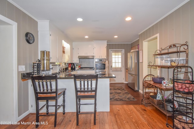 kitchen with ornamental molding, a peninsula, dark countertops, stainless steel appliances, and wood finished floors