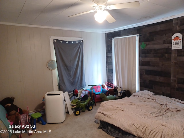 carpeted bedroom featuring wooden walls and a ceiling fan