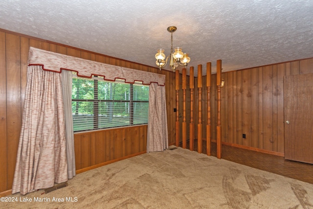 empty room featuring a chandelier, carpet floors, and wood walls