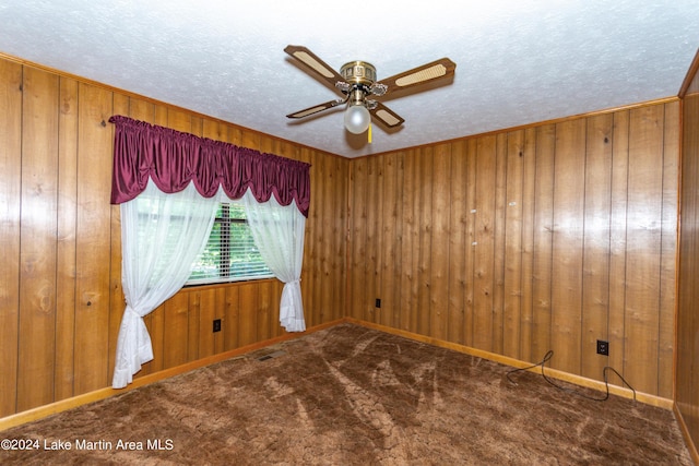 carpeted spare room with a textured ceiling, ceiling fan, and wood walls