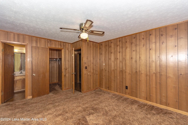 unfurnished bedroom with carpet, wood walls, ensuite bathroom, ceiling fan, and a closet