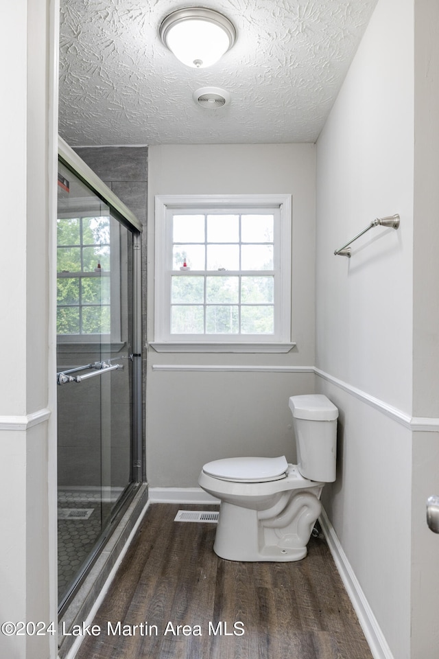 bathroom featuring hardwood / wood-style floors, a textured ceiling, toilet, and a shower with door