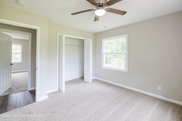 unfurnished bedroom featuring multiple windows, ceiling fan, a closet, and light colored carpet