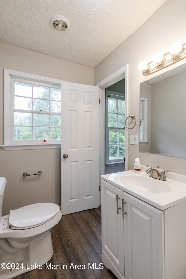 bathroom featuring wood-type flooring, a textured ceiling, toilet, and a healthy amount of sunlight