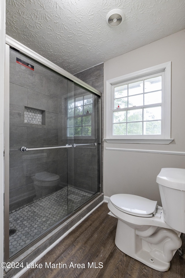 bathroom featuring a textured ceiling, hardwood / wood-style flooring, toilet, and an enclosed shower