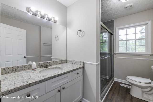 bathroom featuring hardwood / wood-style floors, a textured ceiling, toilet, vanity, and a shower with shower door