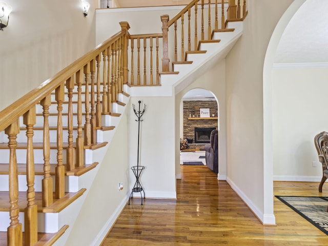 stairway with a stone fireplace, wood-type flooring, a high ceiling, and ornamental molding