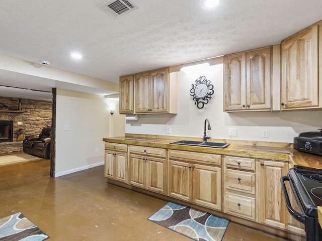 kitchen featuring black range with electric stovetop, a textured ceiling, sink, butcher block countertops, and a stone fireplace