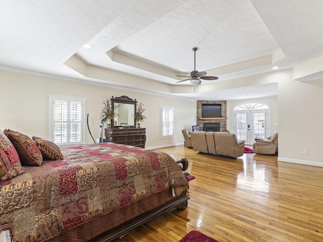 bedroom featuring a tray ceiling, multiple windows, ceiling fan, and light hardwood / wood-style flooring