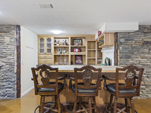 bar with concrete flooring, a textured ceiling, and light brown cabinetry