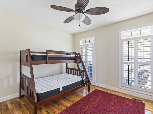 bedroom featuring multiple windows, ceiling fan, a textured ceiling, and hardwood / wood-style flooring