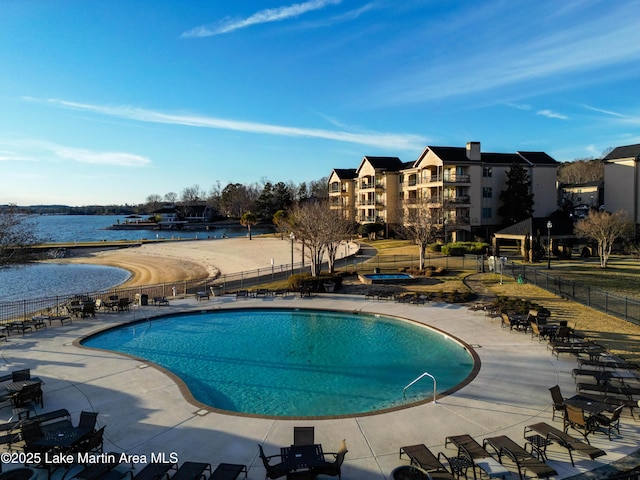 community pool with a patio area, a water view, and fence