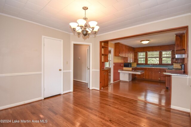 kitchen featuring hanging light fixtures, kitchen peninsula, crown molding, hardwood / wood-style floors, and a chandelier