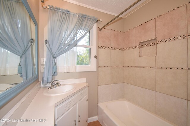 bathroom featuring vanity, a textured ceiling, tiled shower / bath combo, and ornamental molding