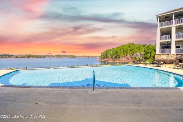 pool at dusk with a patio area, ceiling fan, and a water view