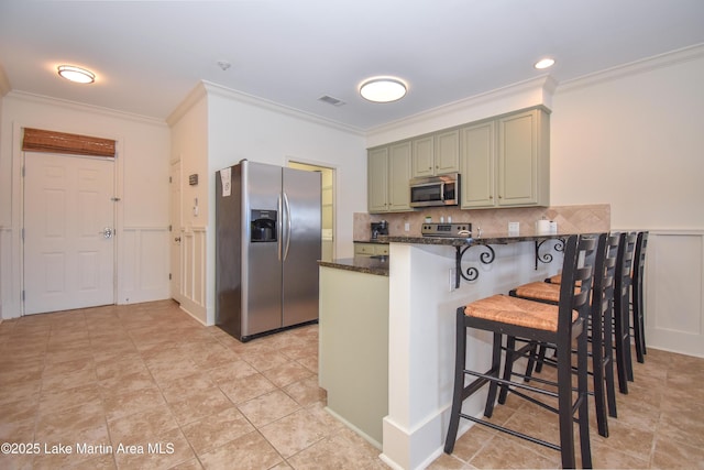 kitchen featuring a breakfast bar, green cabinets, appliances with stainless steel finishes, kitchen peninsula, and dark stone counters