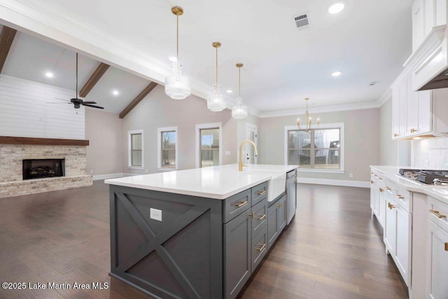 kitchen with white cabinetry, hanging light fixtures, a kitchen island with sink, and lofted ceiling with beams