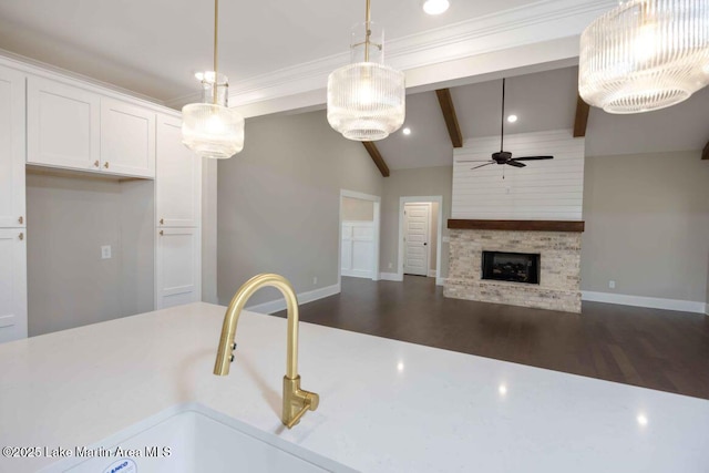 kitchen featuring lofted ceiling with beams, hanging light fixtures, ceiling fan, a fireplace, and white cabinets