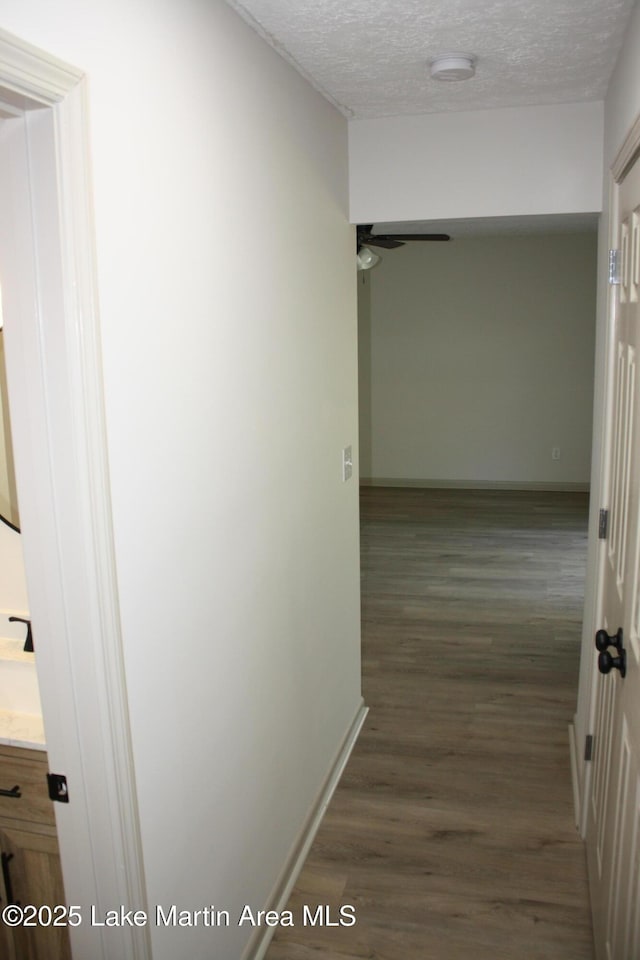 hallway featuring baseboards, dark wood-style flooring, and a textured ceiling