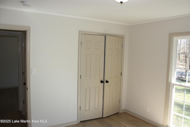 unfurnished bedroom with light wood-style flooring, crown molding, baseboards, and a closet