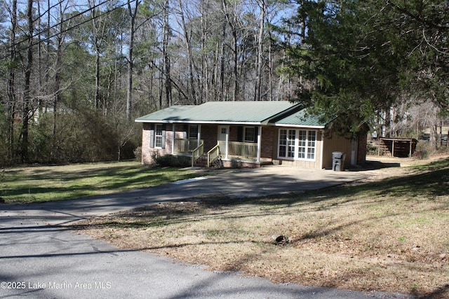 view of front of home with covered porch, driveway, metal roof, and a front yard