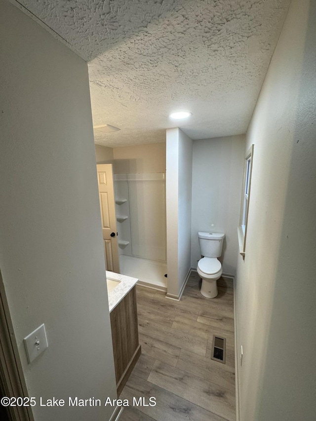 bathroom featuring wood-type flooring, a shower, vanity, toilet, and a textured ceiling