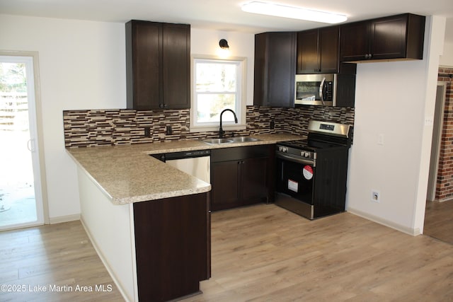 kitchen featuring stainless steel appliances, light wood finished floors, a sink, and dark brown cabinets