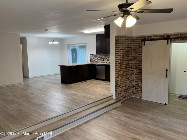 kitchen featuring tasteful backsplash, light hardwood / wood-style flooring, stainless steel dishwasher, kitchen peninsula, and a barn door