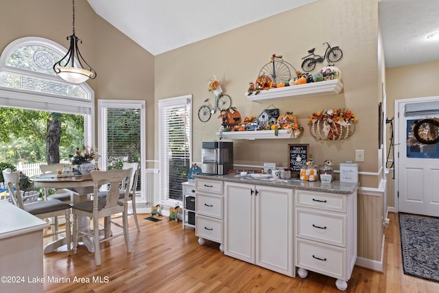 kitchen with a healthy amount of sunlight, hanging light fixtures, white cabinets, and light hardwood / wood-style floors