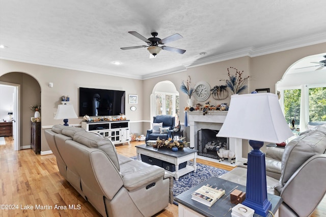 living room featuring ceiling fan, light wood-type flooring, a textured ceiling, a fireplace, and ornamental molding