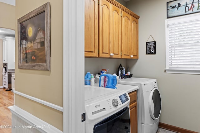 clothes washing area featuring cabinets, washing machine and dryer, and light hardwood / wood-style flooring