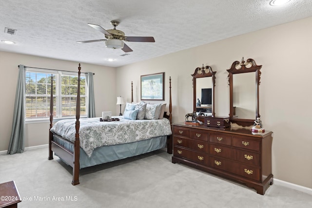 bedroom with ceiling fan, light colored carpet, and a textured ceiling