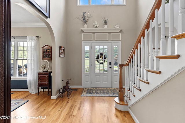 entryway with hardwood / wood-style floors, ornamental molding, a wealth of natural light, and a towering ceiling