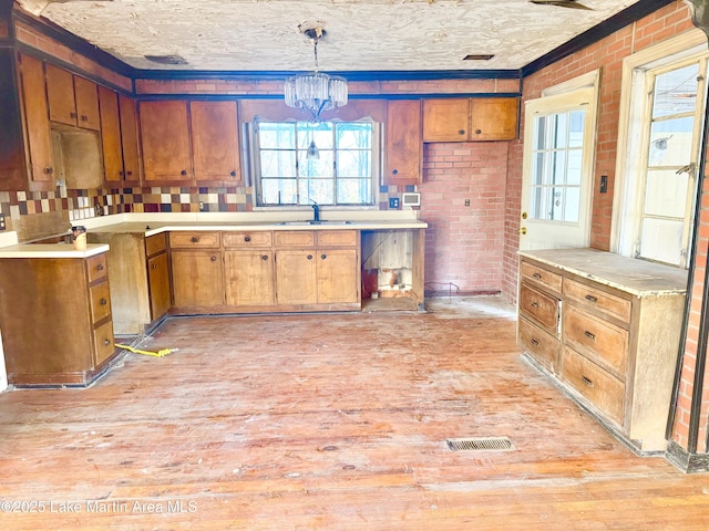 kitchen featuring light wood finished floors, visible vents, an inviting chandelier, brown cabinetry, and brick wall