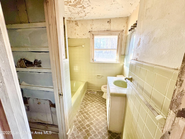 bathroom featuring a wainscoted wall, tile walls, toilet, a bathing tub, and vanity