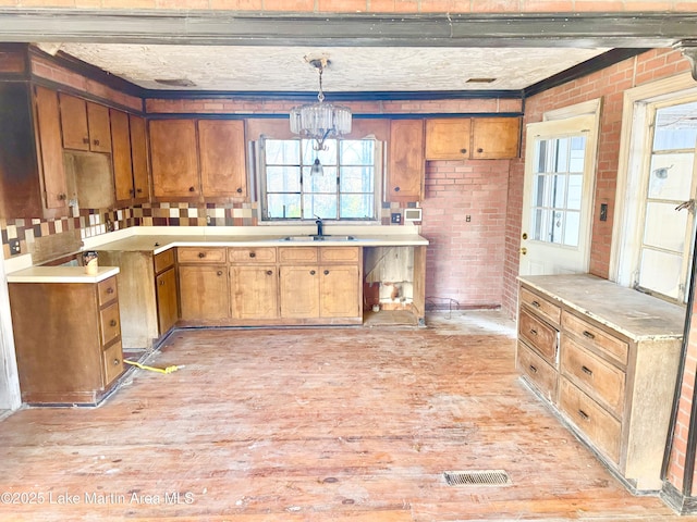 kitchen featuring light wood finished floors, brick wall, light countertops, and a sink