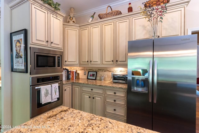 kitchen featuring cream cabinetry, light stone counters, crown molding, and stainless steel appliances