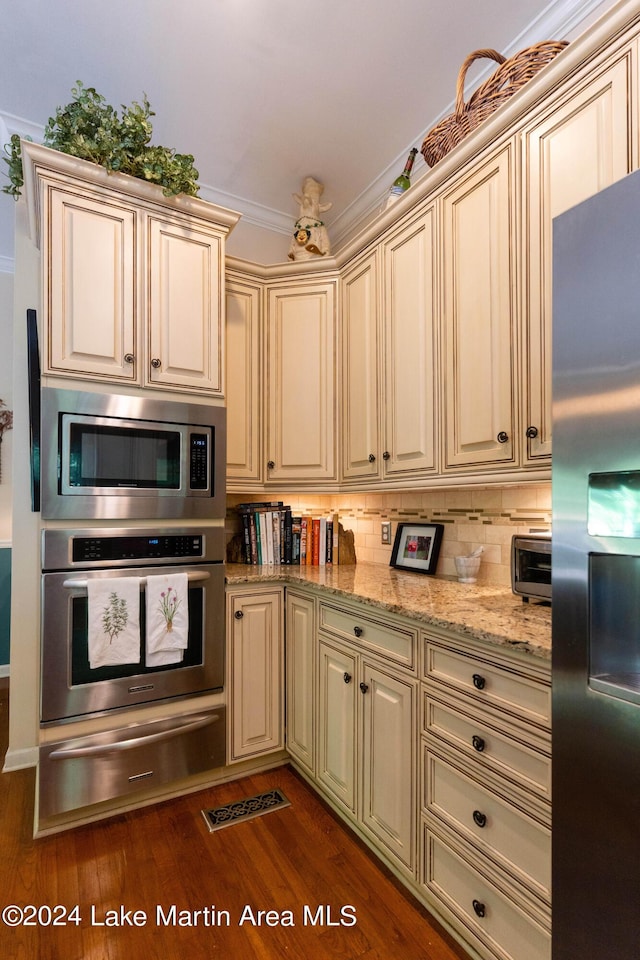 kitchen with dark hardwood / wood-style flooring, light stone countertops, cream cabinets, and stainless steel appliances