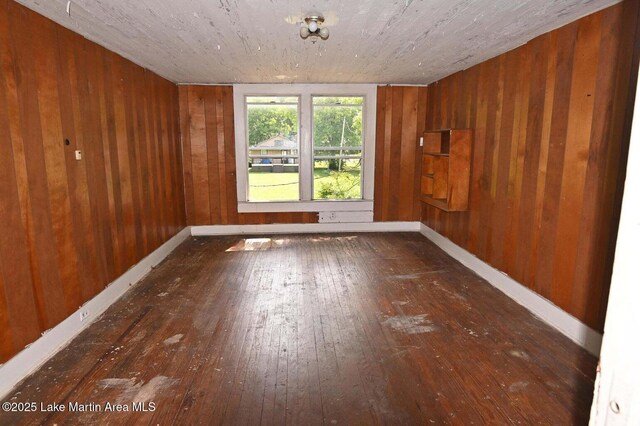 unfurnished room with wood-type flooring, baseboards, and wooden walls