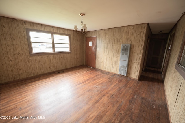spare room with an inviting chandelier, wood finished floors, and a heating unit