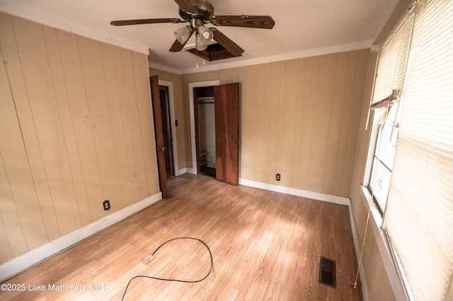 empty room with wood walls, visible vents, baseboards, and light wood-style floors