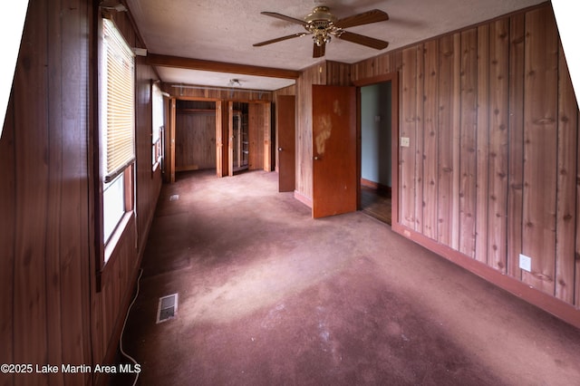 empty room with wood walls, a textured ceiling, ceiling fan, and visible vents