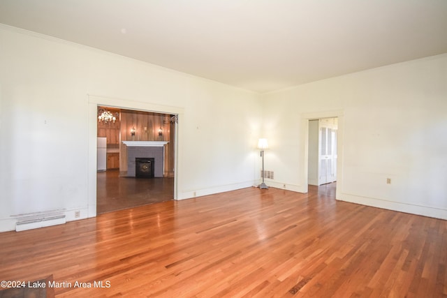 unfurnished room featuring a chandelier, wood-type flooring, a brick fireplace, and crown molding